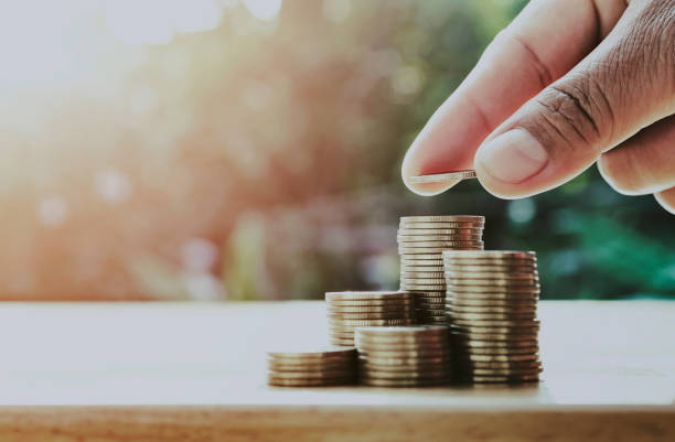 saving money hand putting coins on stack on table with sunshine. concept finance and